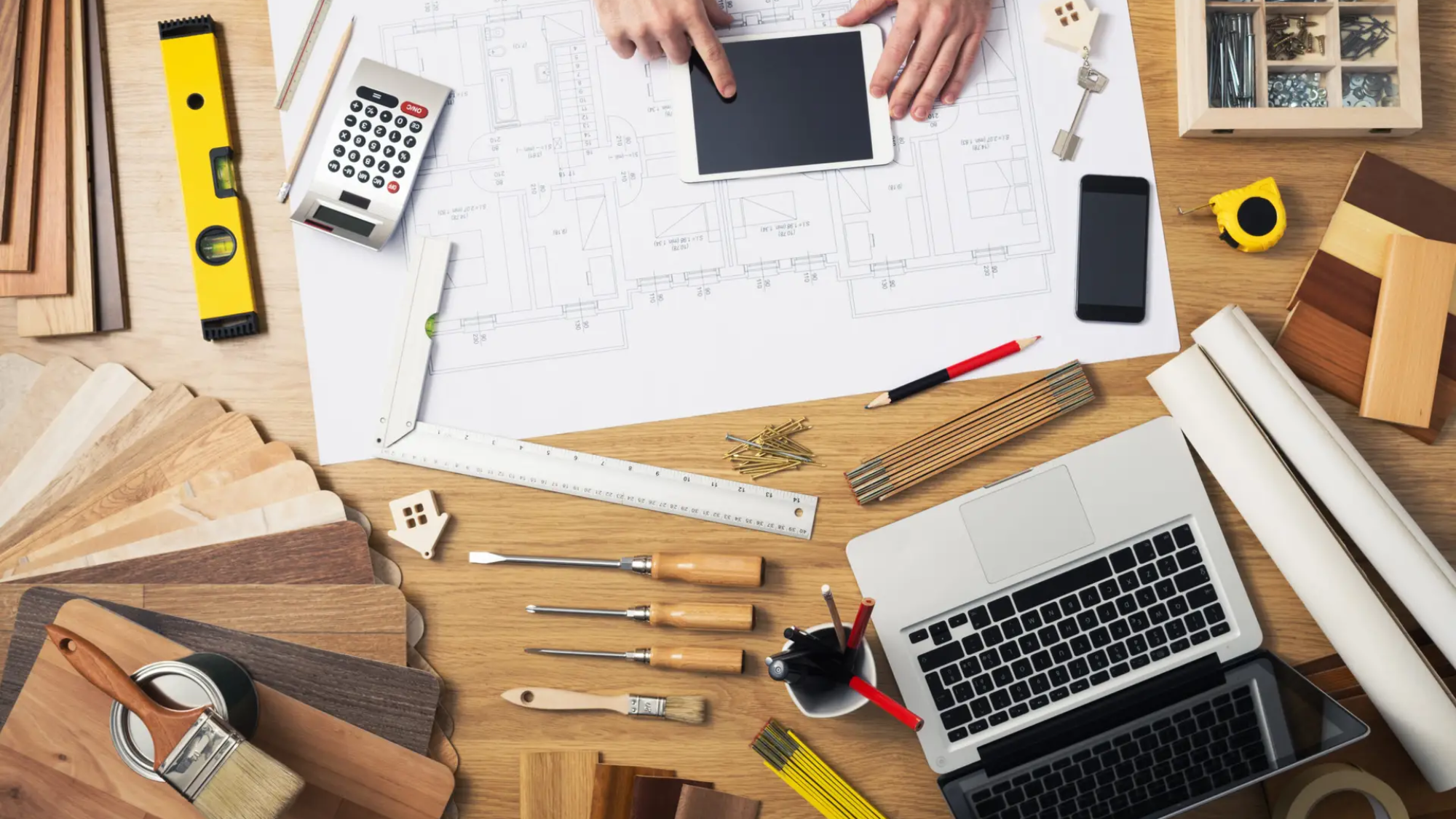 Construction engineer and architect's desk with house projects, laptop, tools and wood swatches top view, male hands using a digital tablet