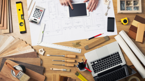 Construction engineer and architect's desk with house projects, laptop, tools and wood swatches top view, male hands using a digital tablet