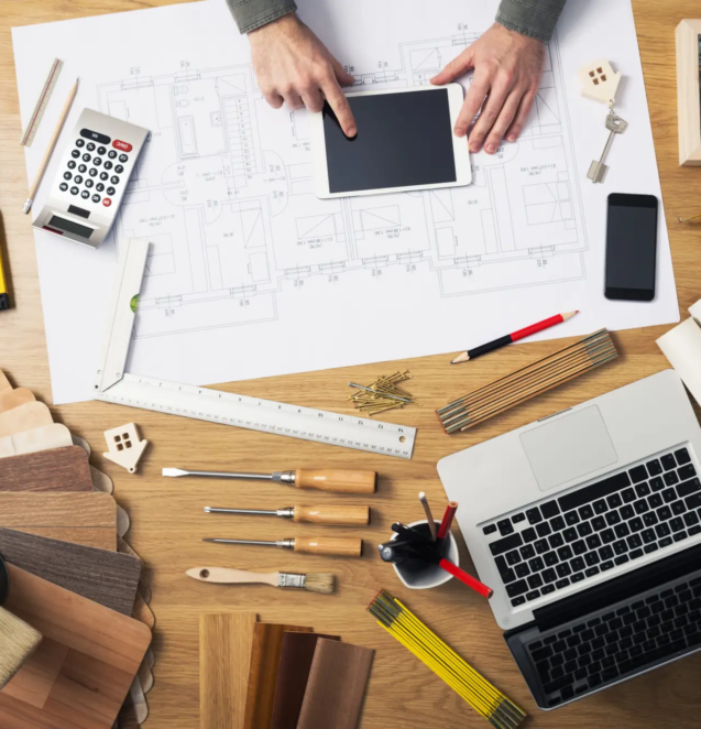 Construction engineer and architect's desk with house projects, laptop, tools and wood swatches top view, male hands using a digital tablet